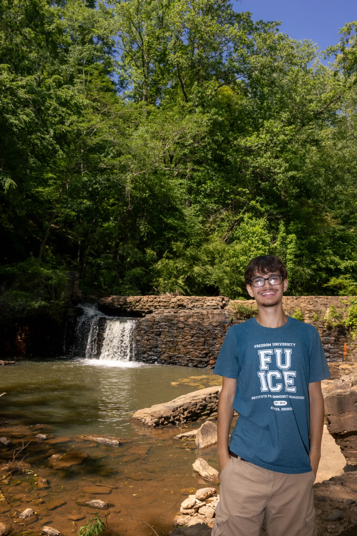 Thomas standing beside a small waterfall surrounded by trees